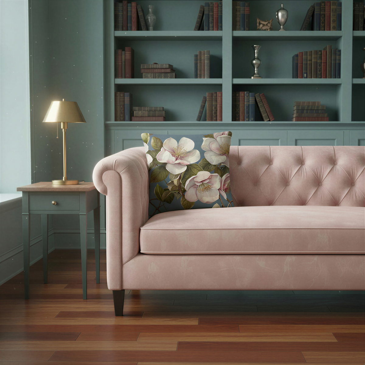 Square decorative cushion featuring large ivory and pale blush-pink blossoms with golden centres, olive-green leaves and brown branches against a muted dusty blue background.