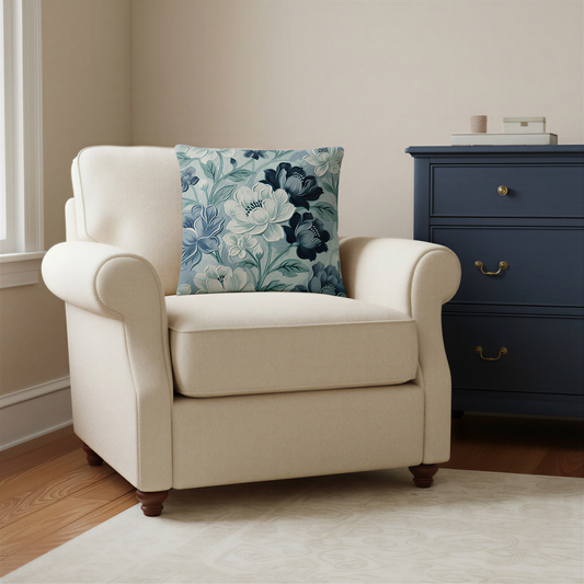 Square decorative cushion featuring large navy blue, slate blue and ivory flowers with pale blue-green leaves against a softly textured blue-grey background.